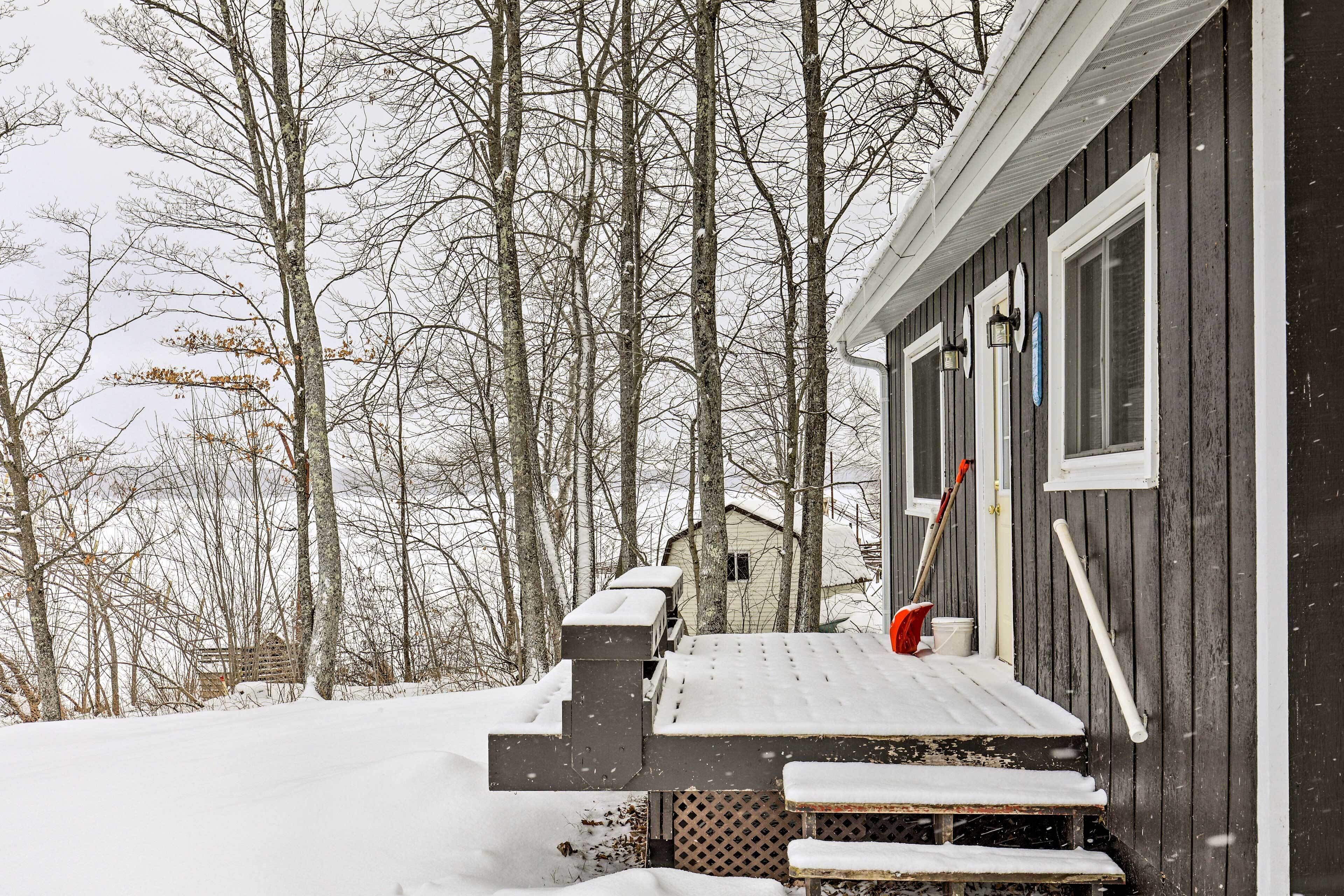 Une cabane en bois avec un porche et des marches enneigés, entourée d’arbres.
