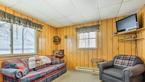 A cozy living room with a plaid sofa, a plaid armchair, a television on a wooden shelf, and a small side table with decorative items. - Tranquil Marenisco Cabin on Lake Gogebic! (Marenisco)