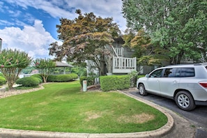 A residential area with a white SUV parked in front of a house with a white fence and a small porch.