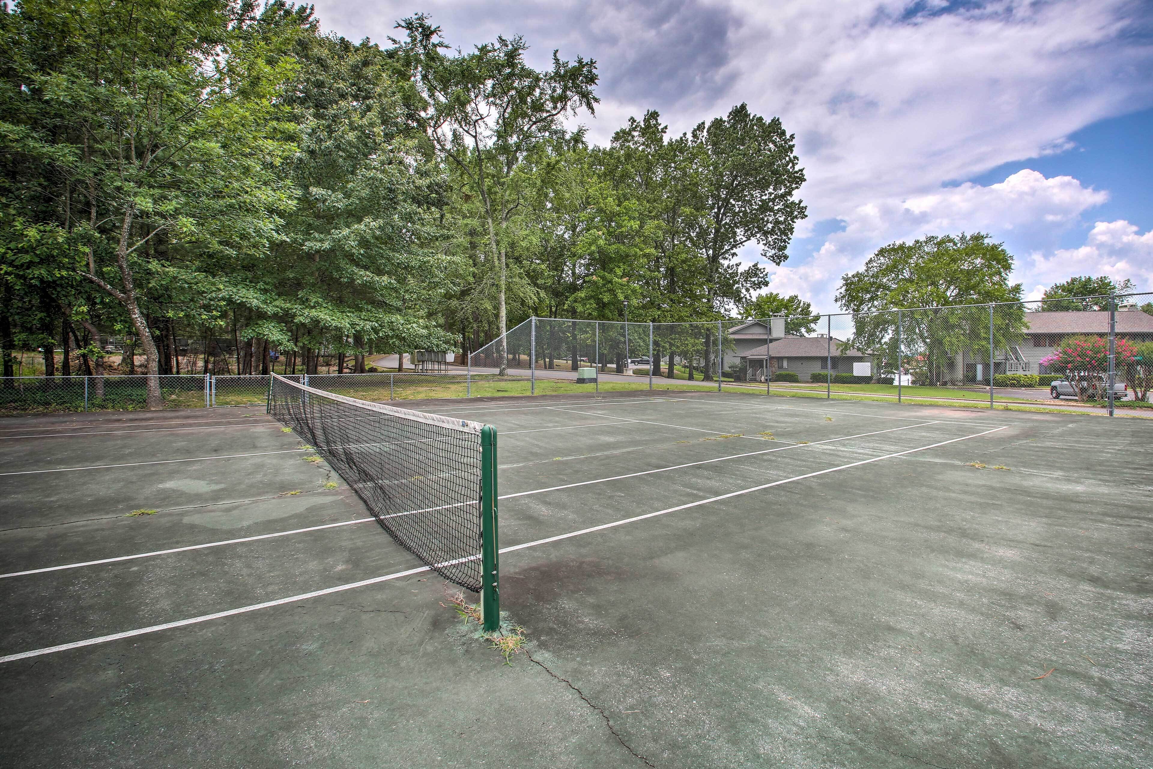 An outdoor tennis court with a net, surrounded by trees and a fence.
