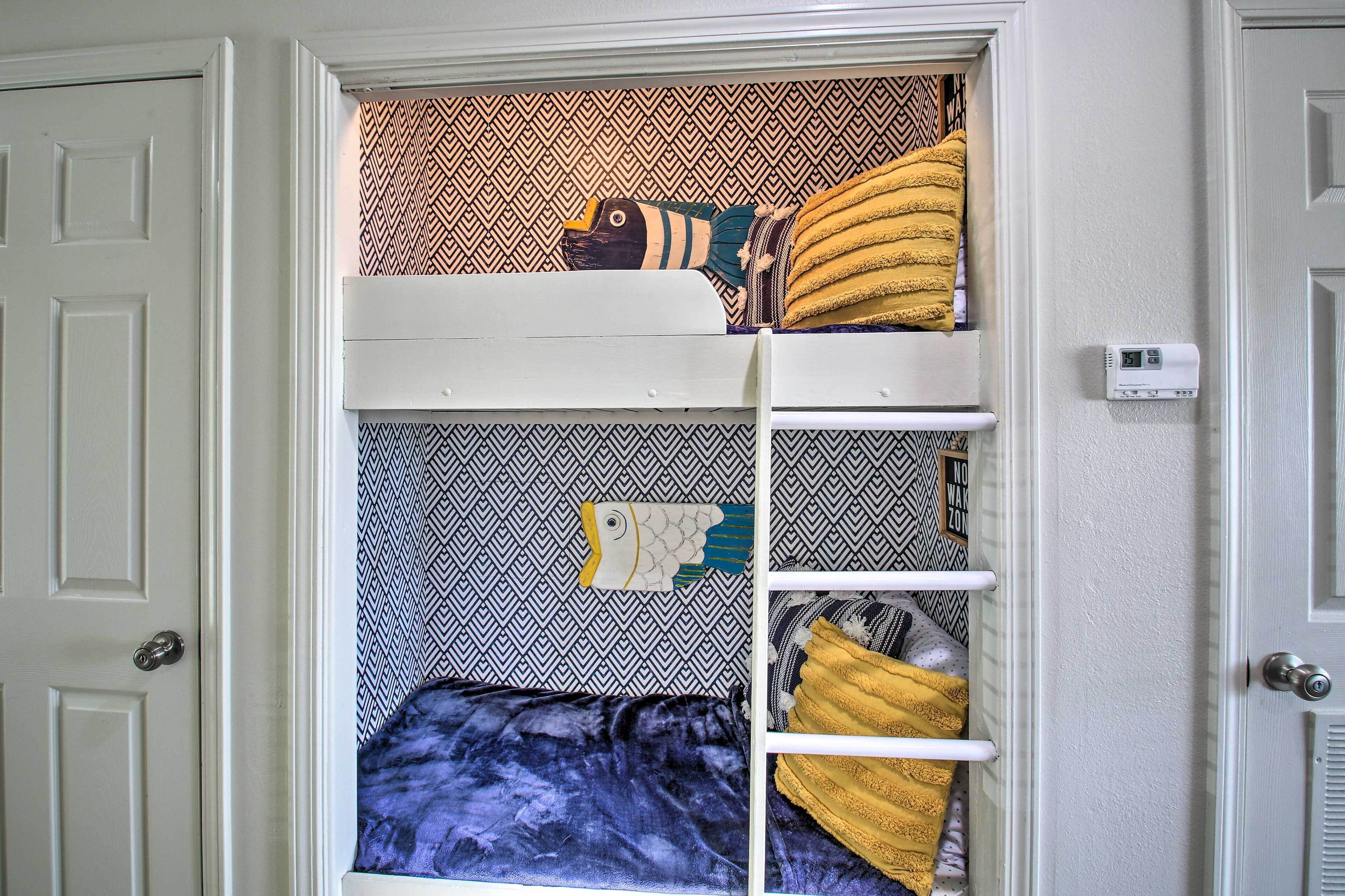 A bunk bed with patterned bedding, a white door, and a thermostat on the wall.