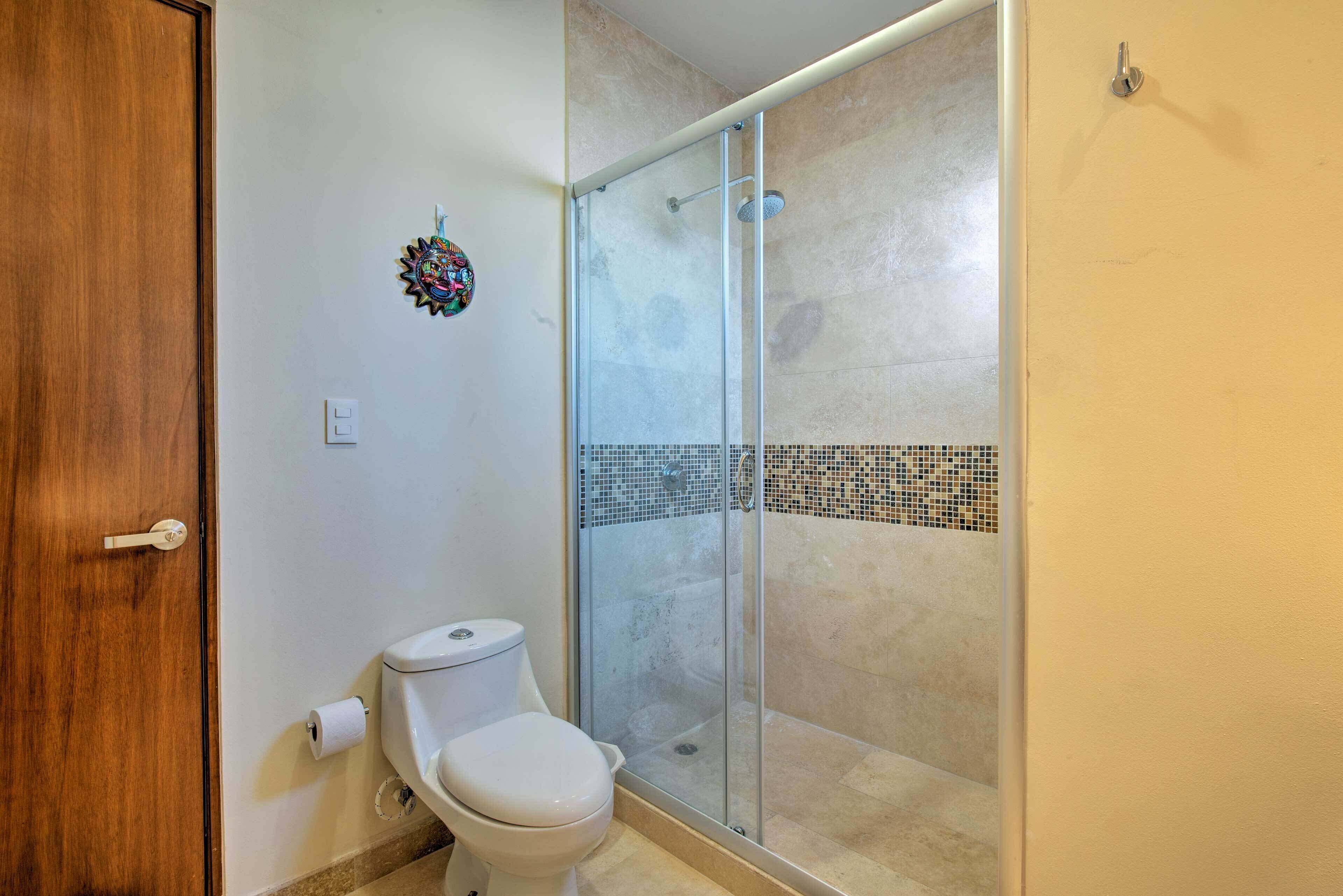 A bathroom with a toilet, a glass shower enclosure, and a mosaic tile border.