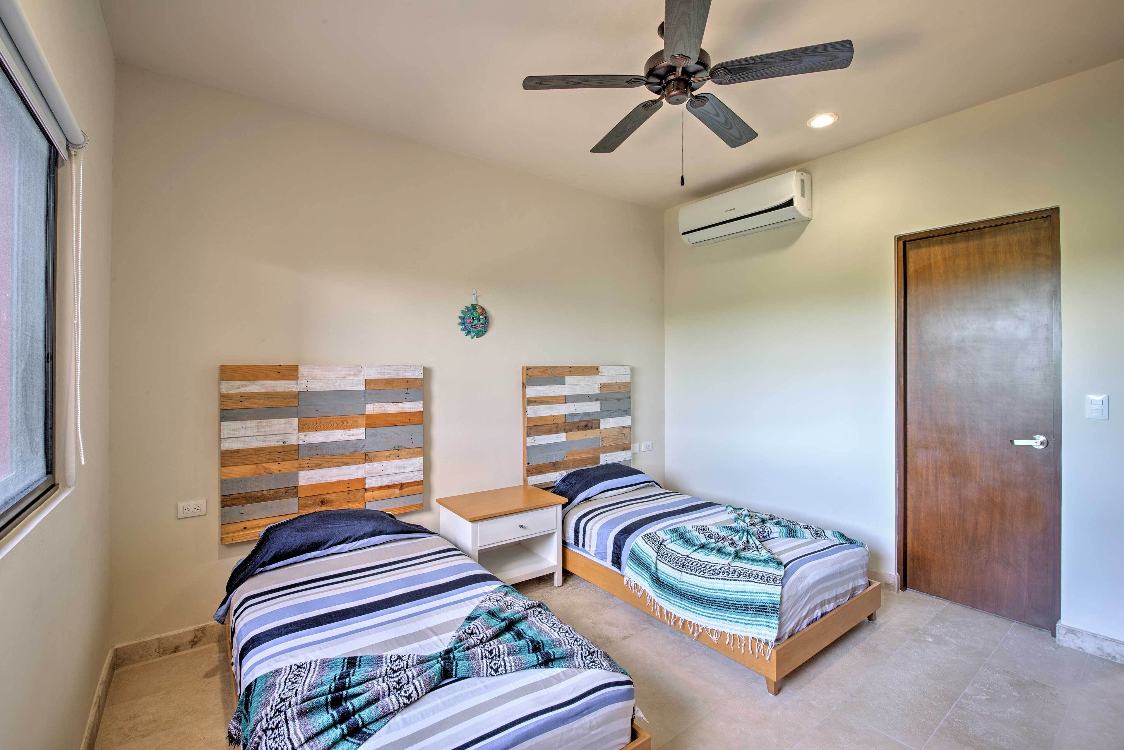 Ein Schlafzimmer mit zwei Betten, einem Deckenventilator, einer Klimaanlage und einer Holztür.