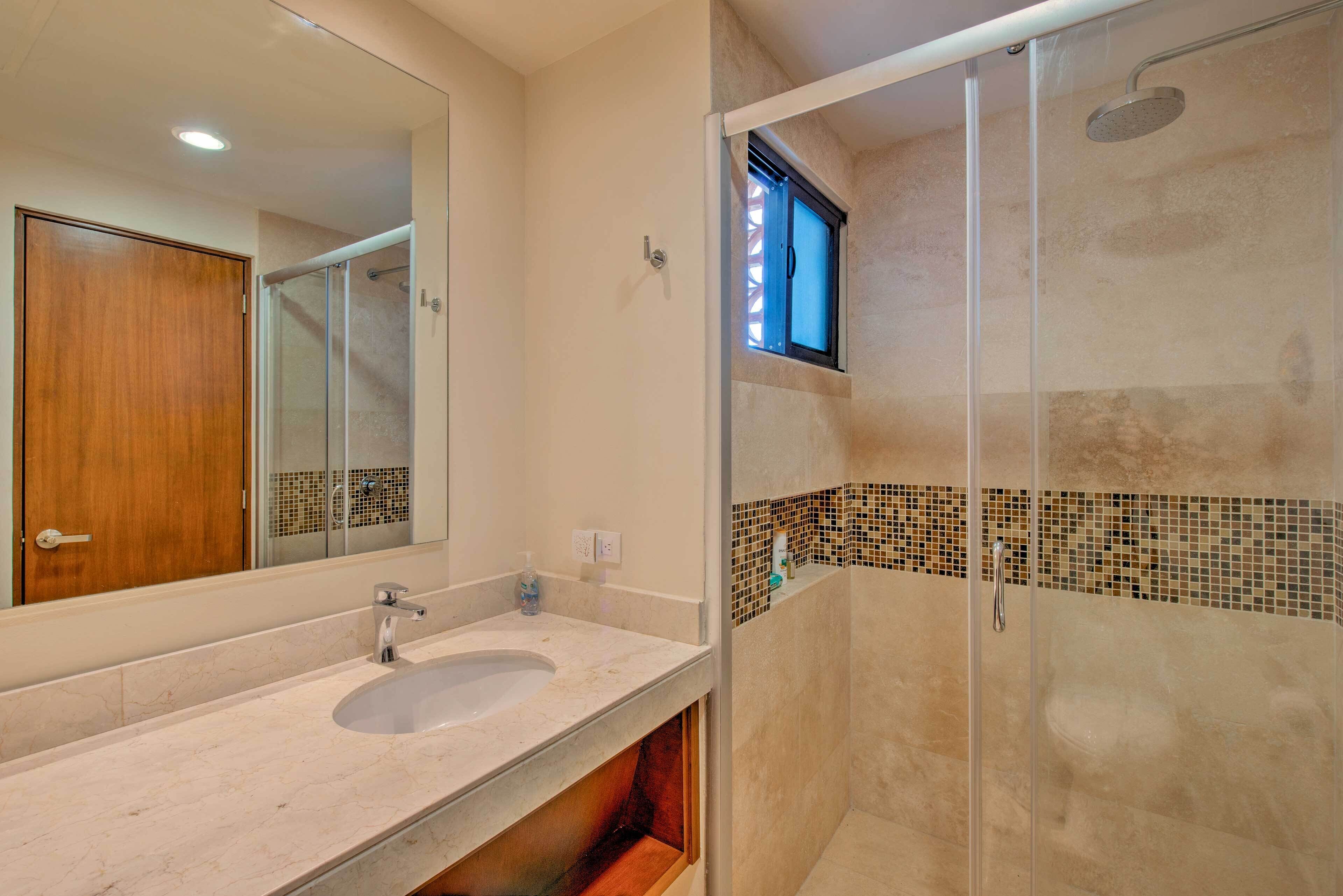 Un baño con lavamanos doble, un espejo grande, ducha con puerta de cristal y una pequeña ventana sobre la ducha.