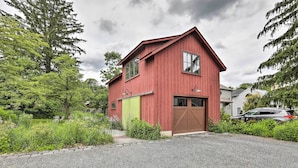 Een rode houten woning met garage, omgeven door groen en een grindpad.