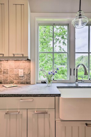 A kitchen with a large window, a stone backsplash, and a vase with flowers.