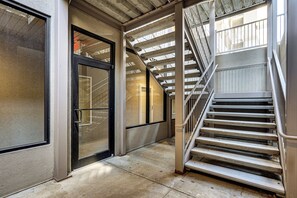 A corridor with a glass door, a staircase, and a metal railing. - Lakefront Patio, Pool Access! Lands End Condo (Osage Beach)