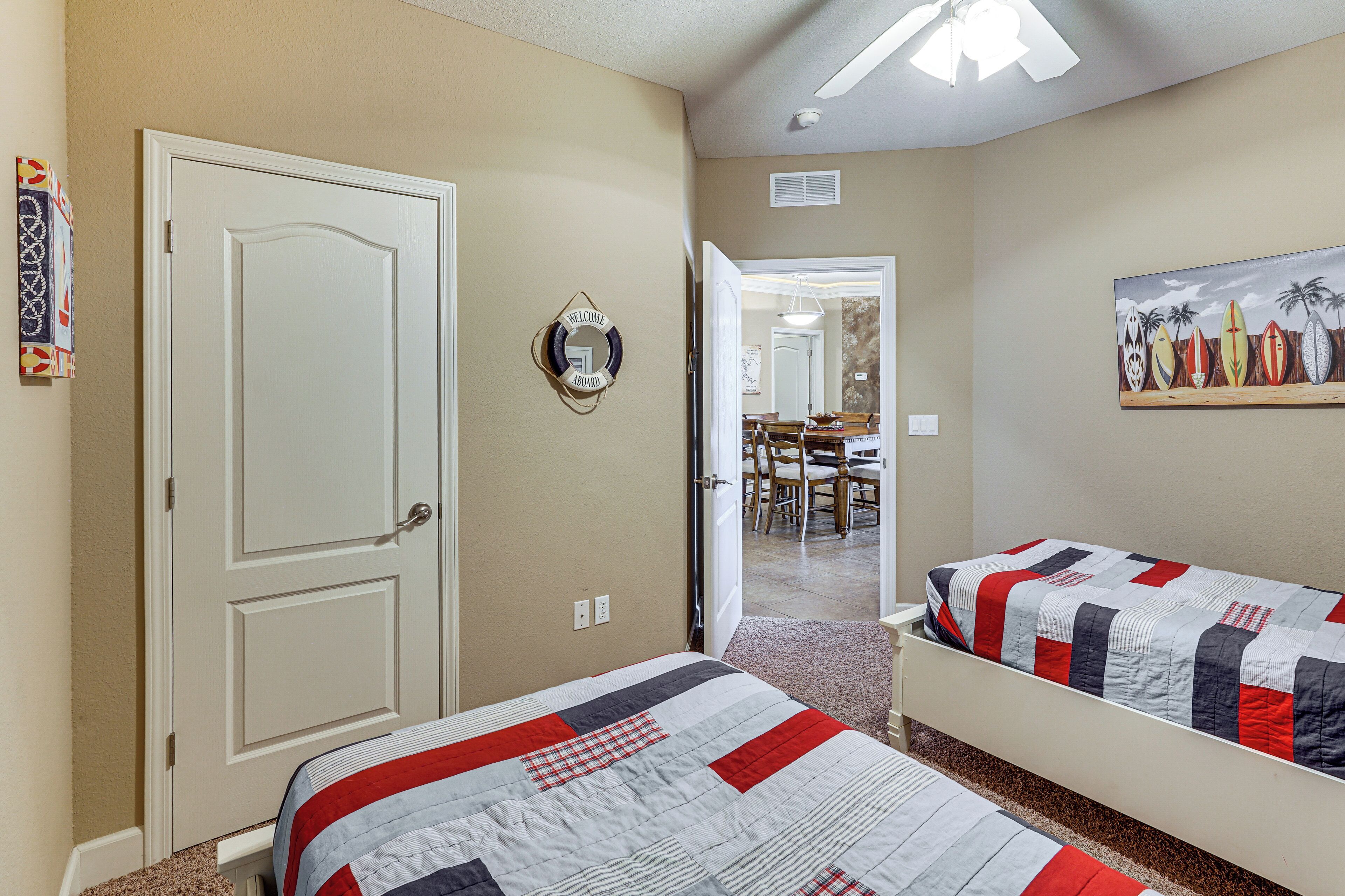 A bedroom with two beds, a door, a welcome sign, and a painting of surfboards.