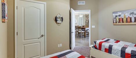 A bedroom with two beds, a door, a welcome sign, and a painting of surfboards.