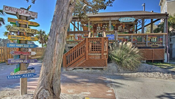 A wooden signpost with multiple directional signs, a wooden staircase leading to a building with a sign reading "Coco's", and a sandy ground area.