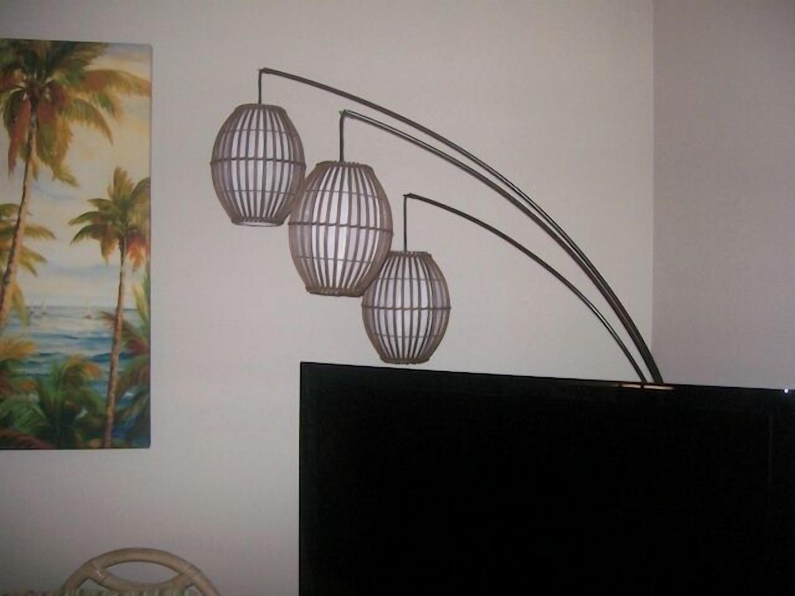 A wall-mounted light fixture with three spherical shades and a painting of a tropical scene.