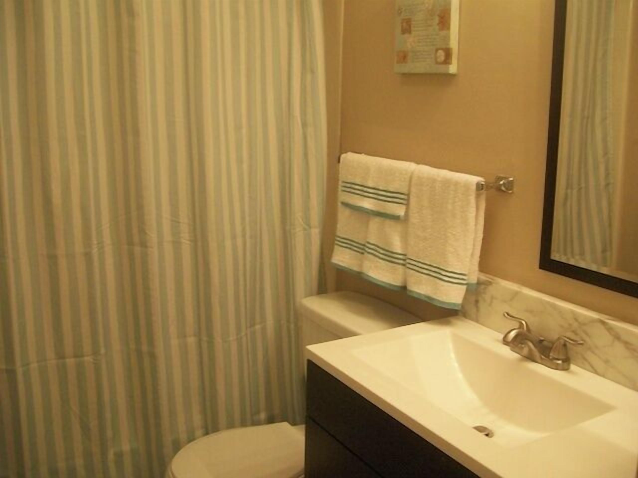 A bathroom with a striped shower curtain, a white toilet, a sink with a marble countertop, and a towel hanging on a towel rack.