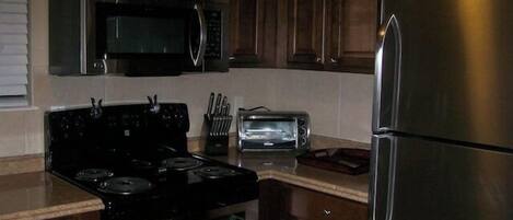 A kitchen with dark wooden cabinets, a stainless steel refrigerator, a microwave, a stove, and a toaster.