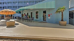 A beachfront hotel with a pool area, outdoor seating, and a palm tree.
