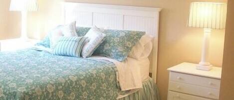 A bedroom with a bed, nightstands, a lamp, a framed picture on the wall, and a floral-patterned bedspread.