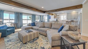 A modern living room with a large sectional sofa, a coffee table, and a view of the kitchen. - Cozy Waterfront Hale Cottage on Long Lake! (Hale)