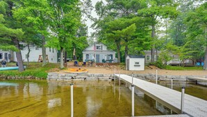 A lakeside cabin with a dock extending into a pond, surrounded by trees and a small deck area. - Cozy Waterfront Hale Cottage on Long Lake! (Hale)