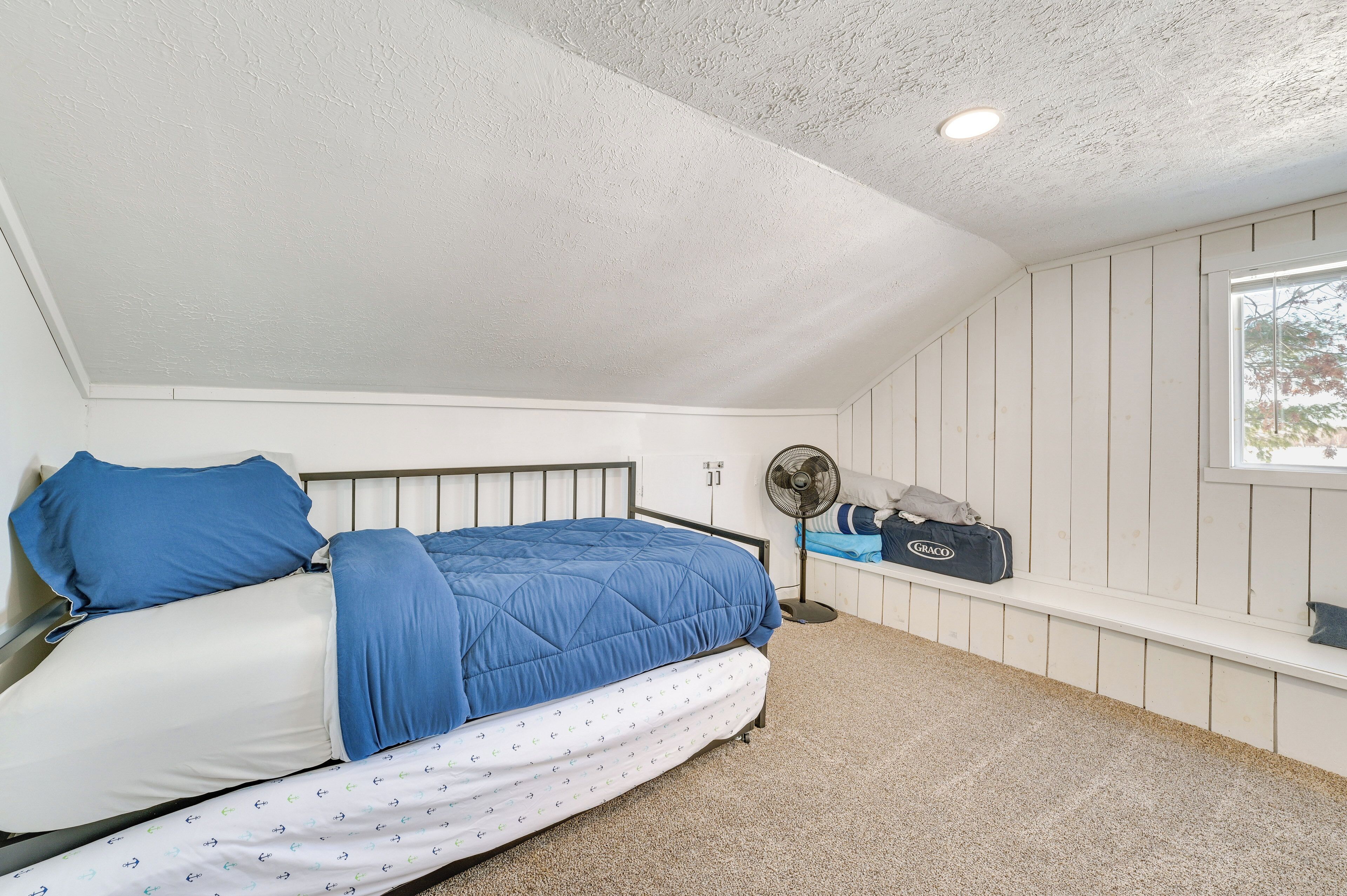 Une chambre à coucher avec un lit, une fenêtre, un ventilateur et un banc.
