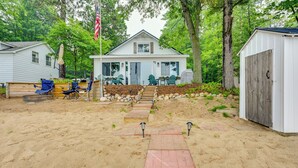 A house with a front porch, a flag, and a sandy yard. - Cozy Waterfront Hale Cottage on Long Lake! (Hale)
