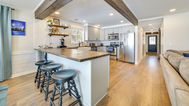 A modern kitchen with a central island, bar stools, and stainless steel appliances. - Cozy Waterfront Hale Cottage on Long Lake! (Hale)