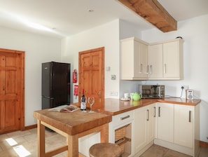Une cuisine avec des meubles de rangement en bois, un réfrigérateur noir, un four à micro-ondes et une table en bois sur laquelle se trouvent un magazine et des verres à vin.