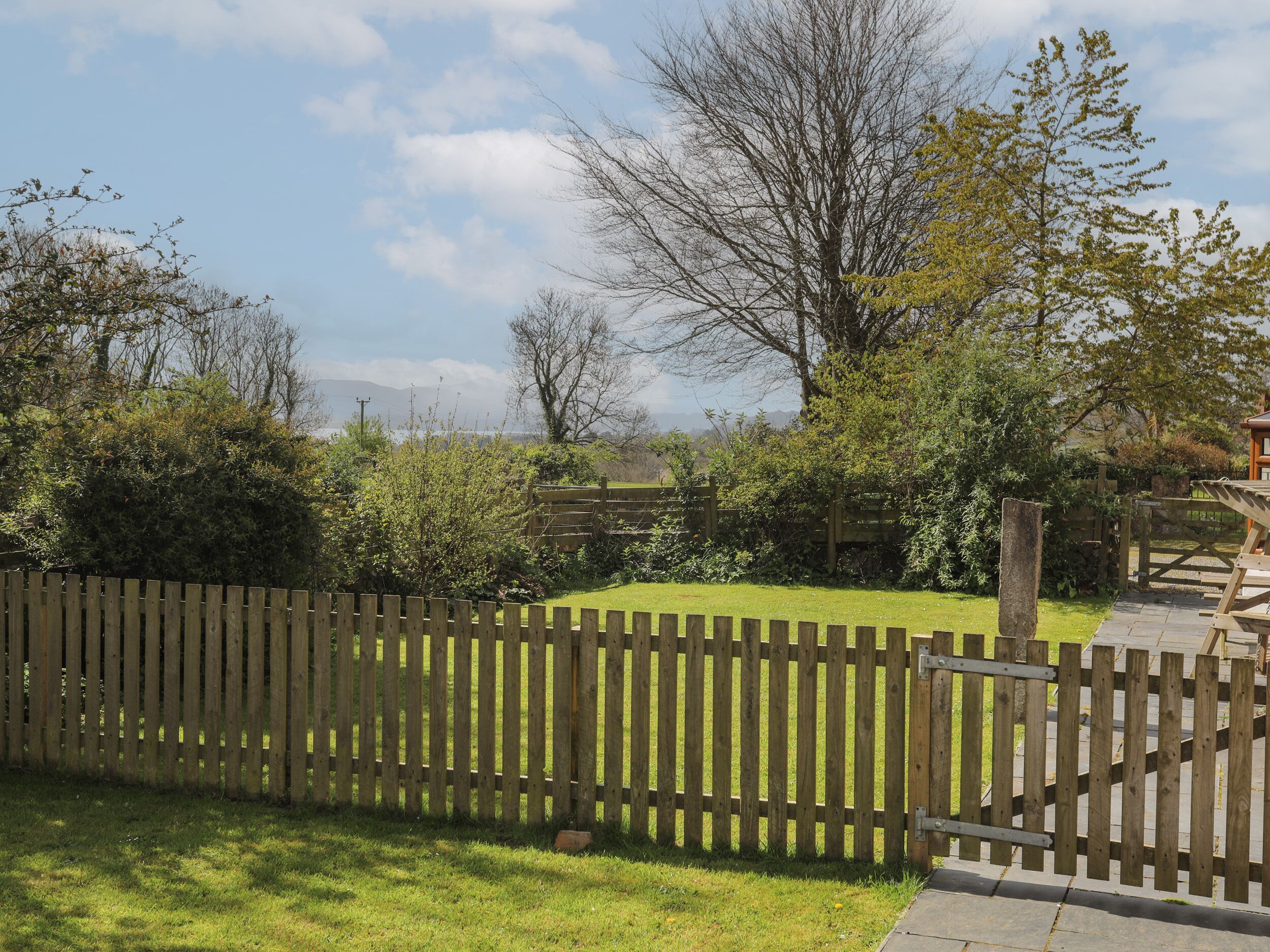 A wooden fence in a garden with a grassy area and trees in the background.