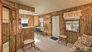 A cabin interior with wooden walls, a dining area with a table and chairs, a sofa, and a door leading outside.