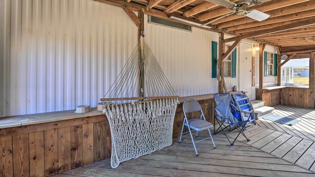A covered porch with a hammock, a folding chair, and a ceiling fan.