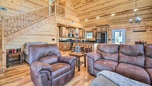 A spacious living area with leather sofas, a wooden staircase, and a kitchen in the background. - Hot Tub & Game Room: Mountaintop Cabin in Murphy! (Murphy)
