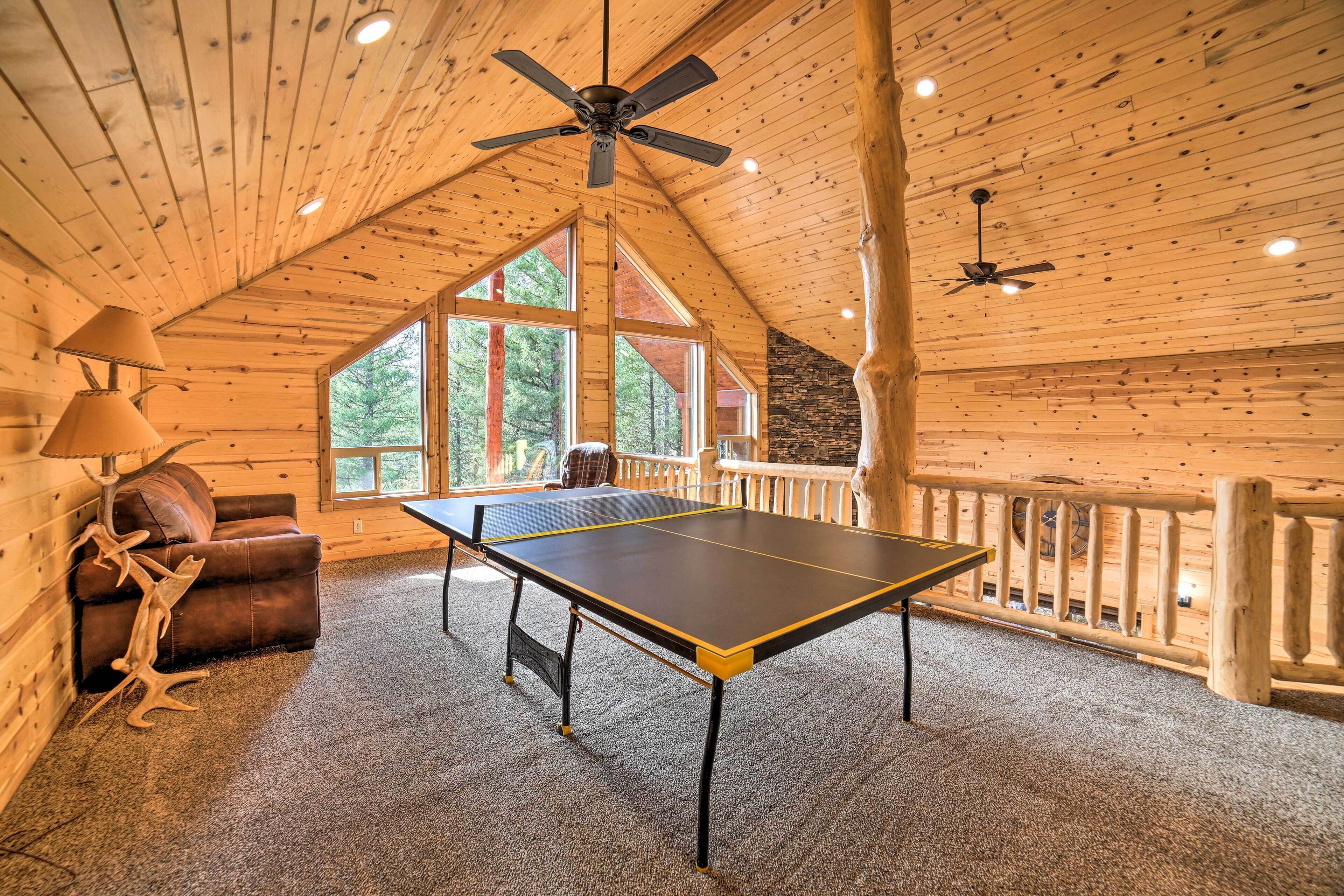 Une table de ping-pong dans une pièce en bois avec un plafond en pente, un canapé en cuir marron et une lampe.