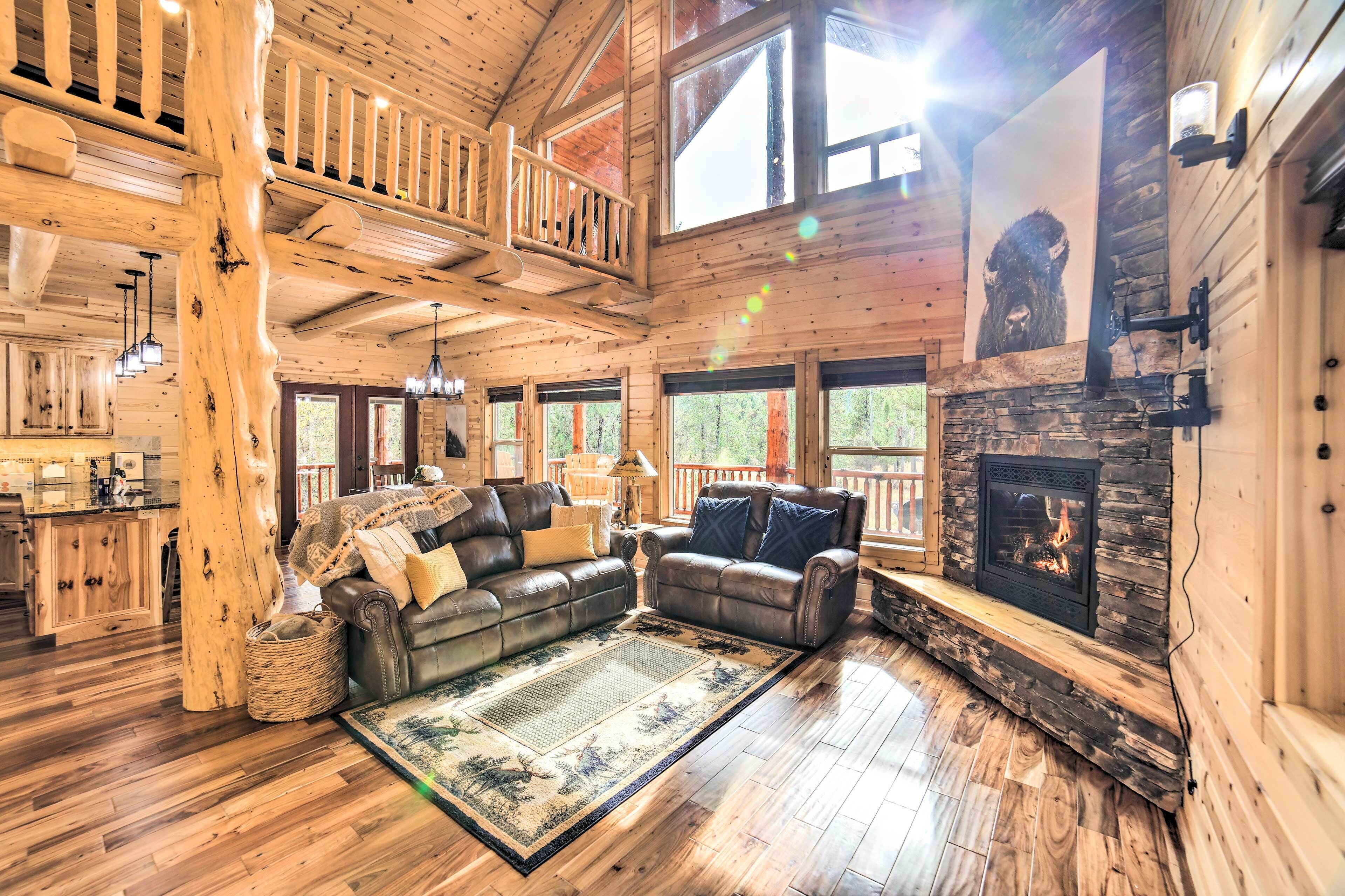 A spacious log cabin interior with a fireplace, leather sofas, a dining area, and a balcony.