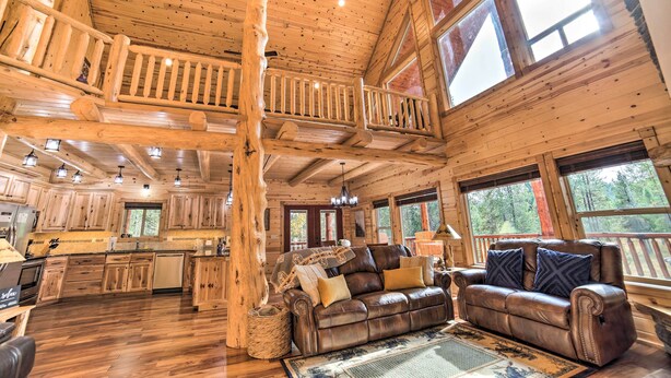 Ein geräumiges Blockhaus-Interieur mit hohen Decken, Holzböden, einem Essbereich, einem Wohnzimmer mit Ledersofa und großen Fenstern mit Blick auf den umliegenden Wald.