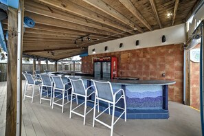 A covered outdoor bar area with a mosaic-tiled bar counter and white metal chairs. - Community Perks + Beach: North Myrtle Beach Condo (North Myrtle Beach)