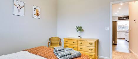 Une chambre à coucher comprenant un lit, une commode en bois, une chaise et deux tableaux accrochés au mur.
