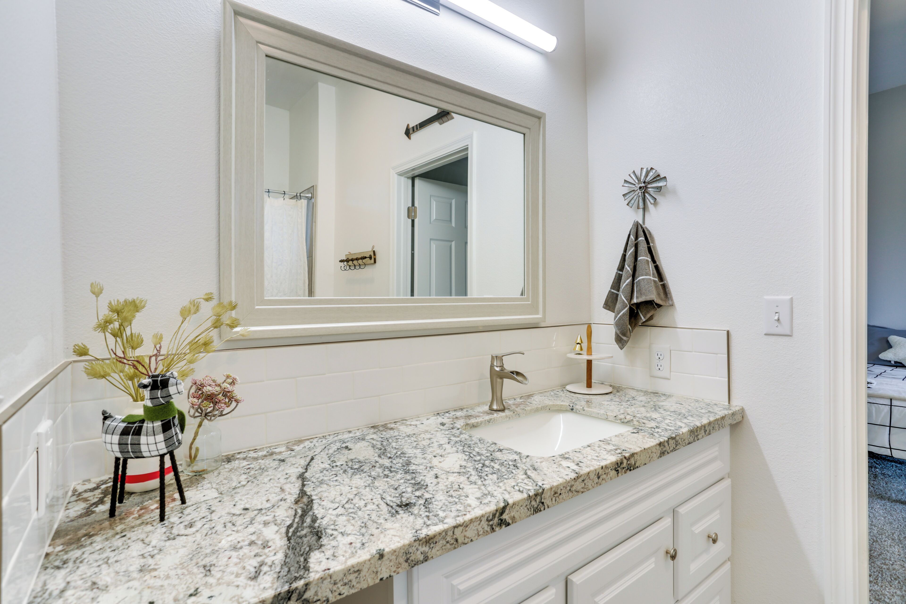 A bathroom with a marble sink, white cabinets, a large mirror, and a towel rack.