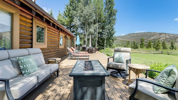 A wooden deck with a sofa, chairs, and a table, overlooking a grassy area and trees. - Snowmass Home w/ Hot Tub, Fireplace, & Mtn Views! (Snowmass)