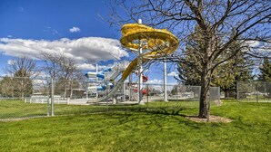 A playground with a yellow spiral slide and a tree in the foreground.
