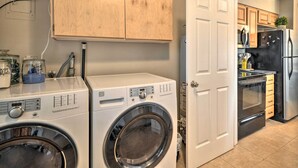 A laundry area with a front-loading washer and dryer, wooden cabinets, a white door, and a kitchen with a refrigerator and oven.