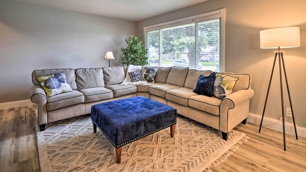 A living room with a sectional sofa, a blue ottoman, a floor lamp, and a window with blinds.