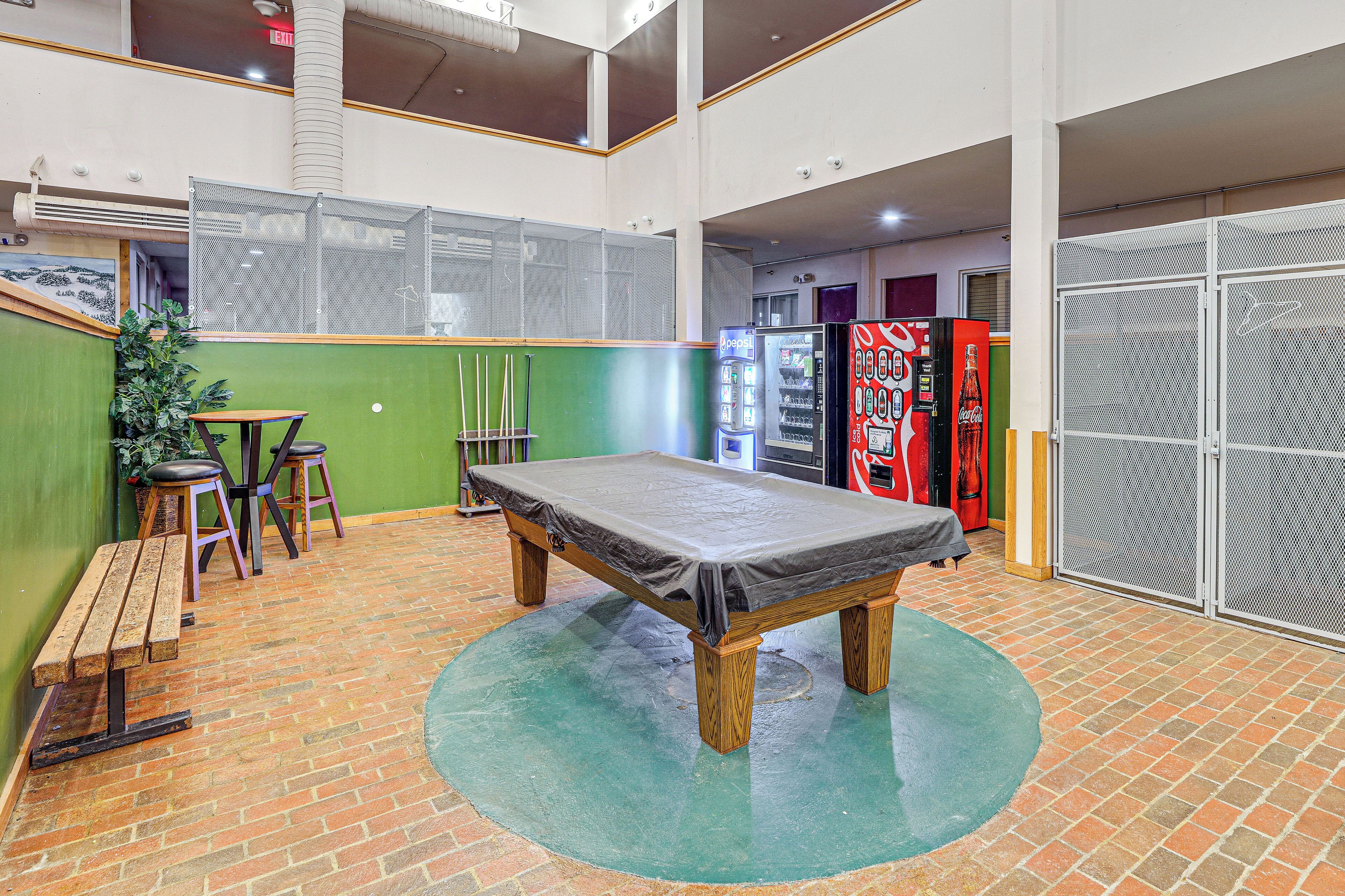A billiards table in a room with a brick floor, green walls, and a high ceiling.