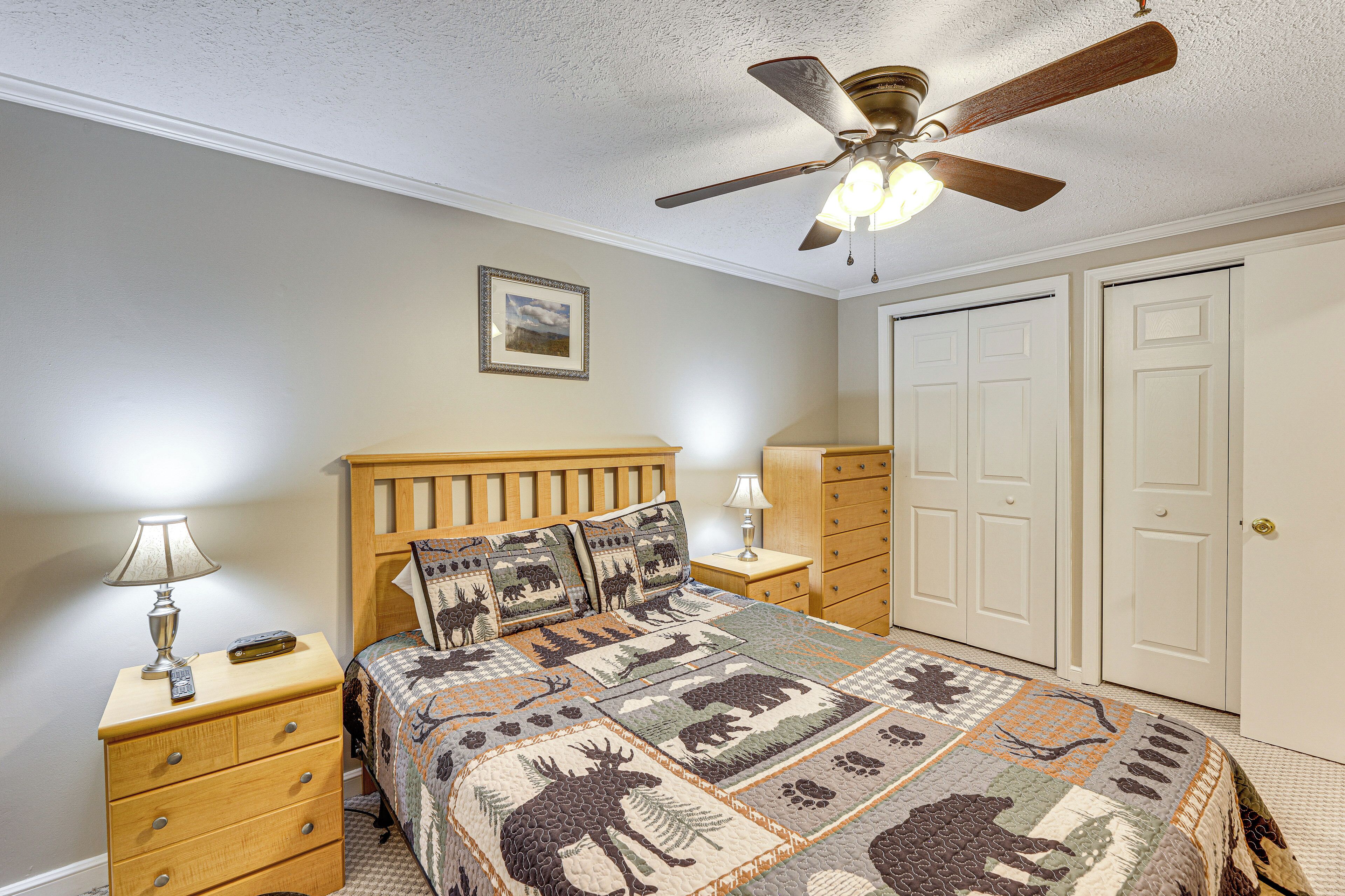 A bedroom with a wooden bed, a ceiling fan, a nightstand with a lamp, and a dresser.