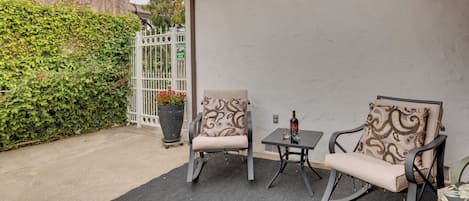 Un patio al aire libre con dos mecedoras y una mesita, rodeado por un muro blanco y una valla de madera.