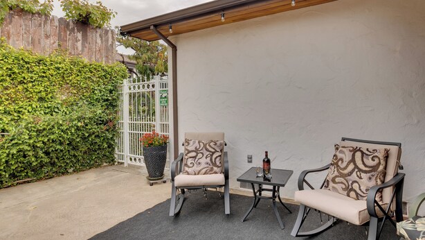 An outdoor patio area with two rocking chairs and a small table, surrounded by a white wall and a wooden fence. - Downtown Jackson Gem! w/ Patio, Pool Table & Games (Jackson)