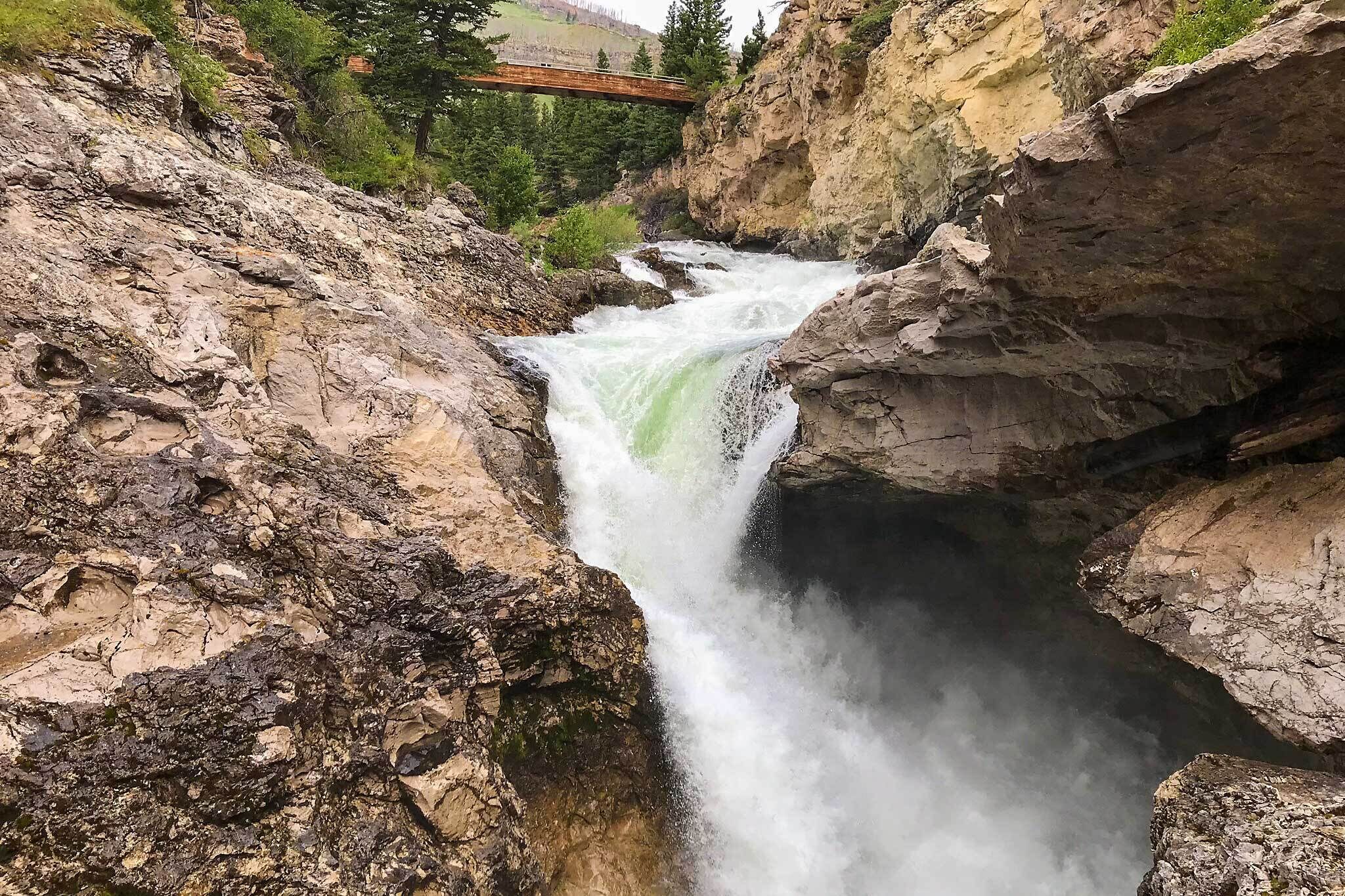 A waterfall cascading down rocky terrain with a bridge in the background.
