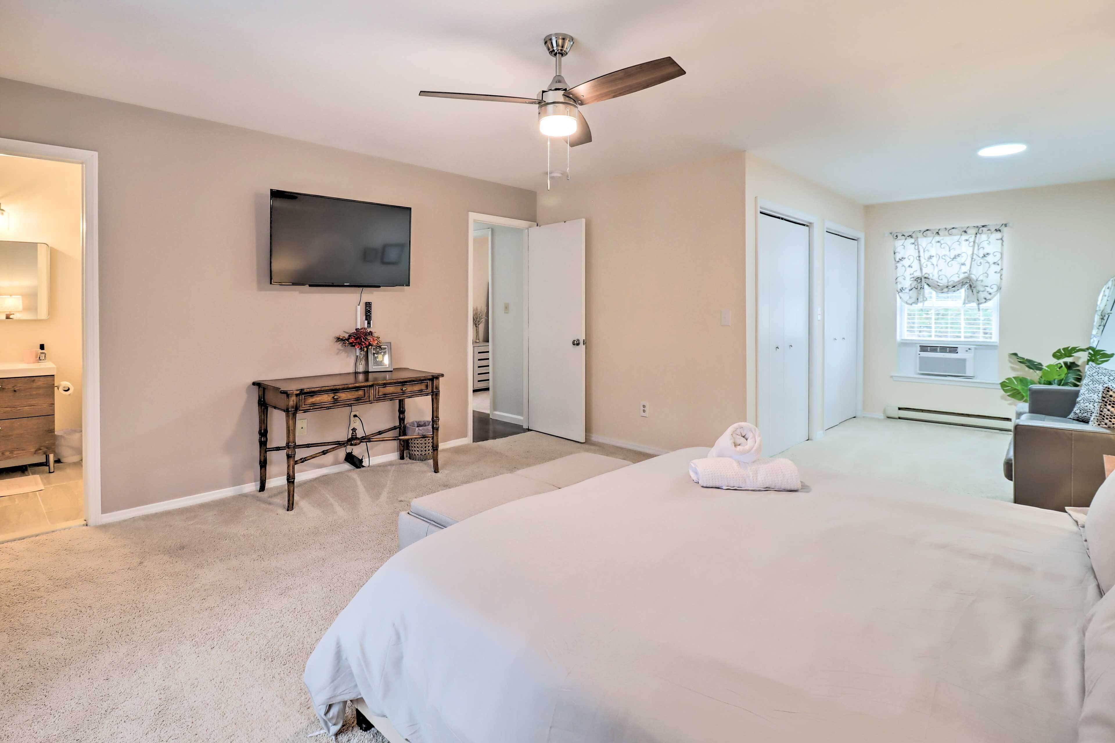 A bedroom with a bed, a ceiling fan, a TV, a desk, and a window with curtains.