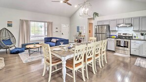 A modern kitchen with stainless steel appliances, a dining area with a wooden table and white chairs, and a living area with a blue sofa and a hanging chair. - Gas Grill, Lake Access: Scenic Poconos Retreat! (East Stroudsburg)