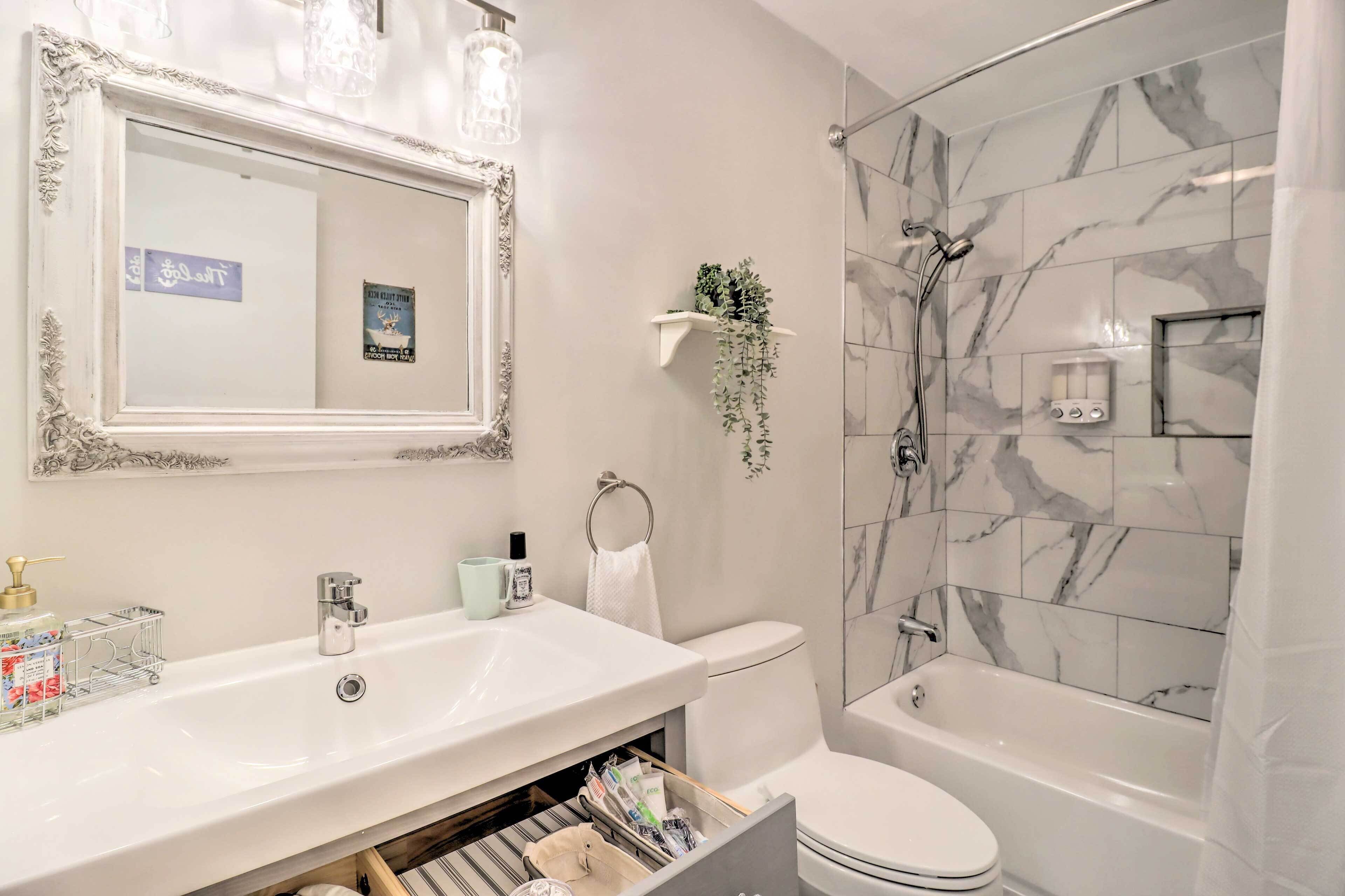 Een badkamer met een wit wastafelmeubel, een spiegel met een sierlijk frame, een douche met marmeren tegels, en een toilet.