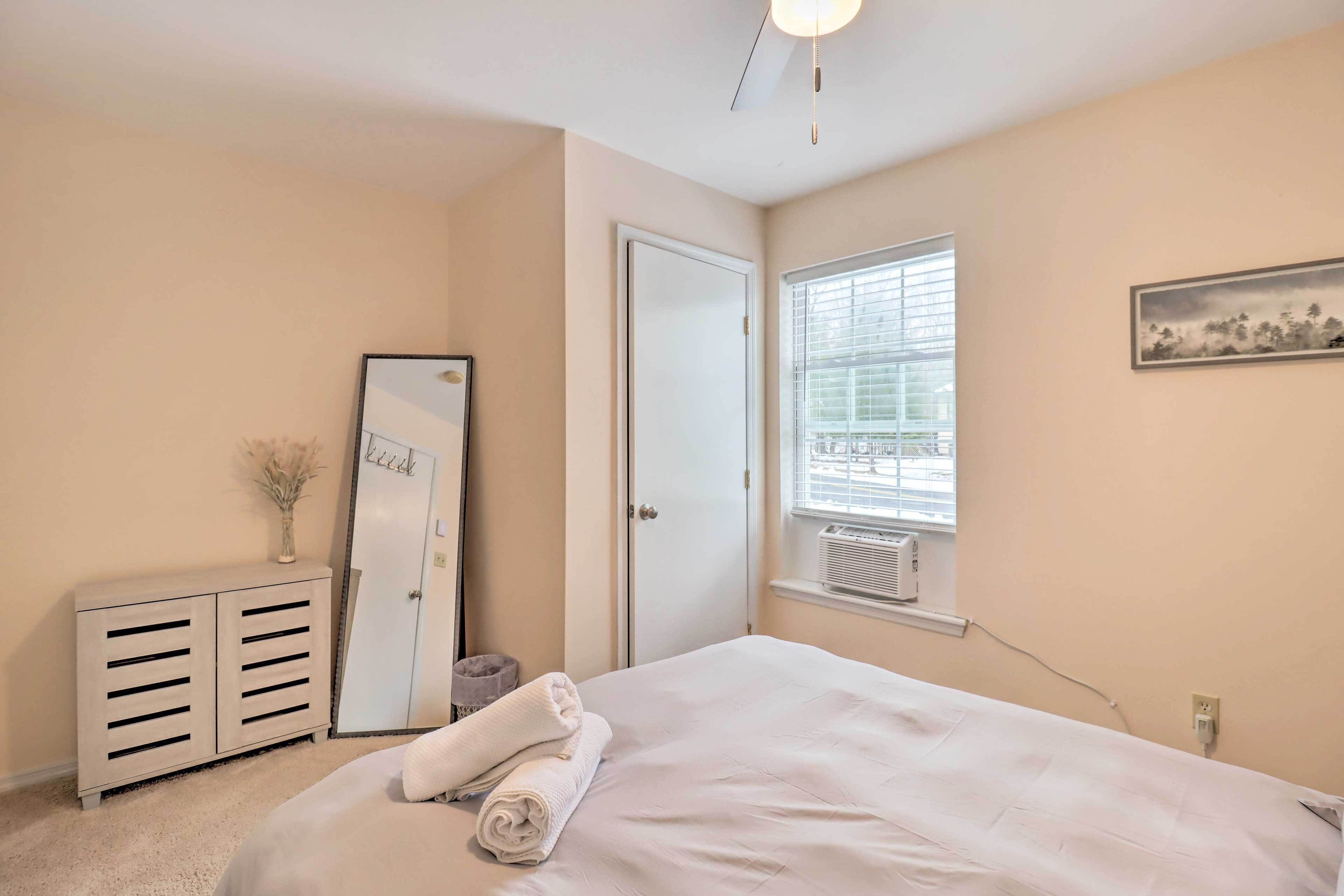 Une chambre à coucher comprenant un lit, une armoire, un miroir, une fen être avec des stores et un tableau accroché au mur.