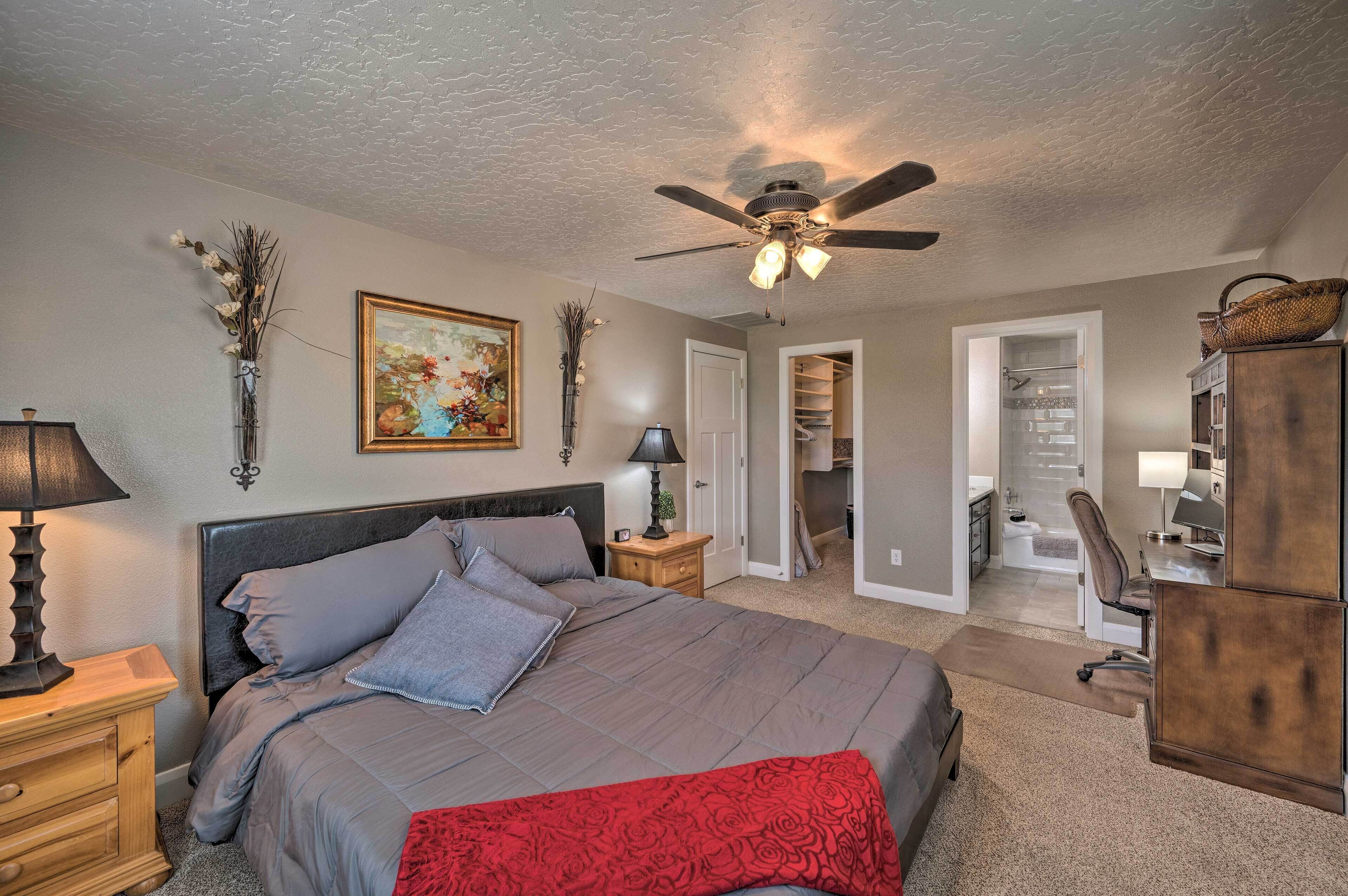 A bedroom with a bed, a ceiling fan, a nightstand, a dresser, and a door leading to a bathroom.