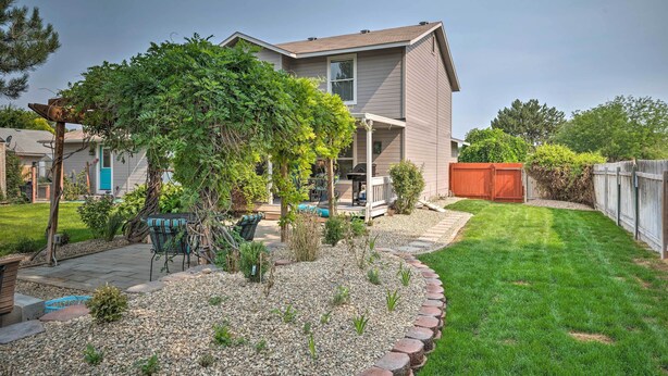 A residential backyard with a house, a patio with a table and chairs, a small tree, and a well-maintained lawn. - Idyllic Nampa Family Home With Hot Tub & Fire Pit! (Nampa)